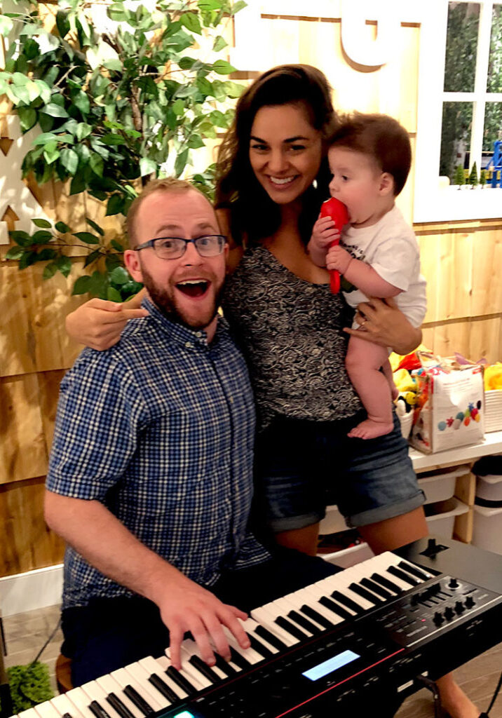 smiling male and female musicians holding a baby with a maraca