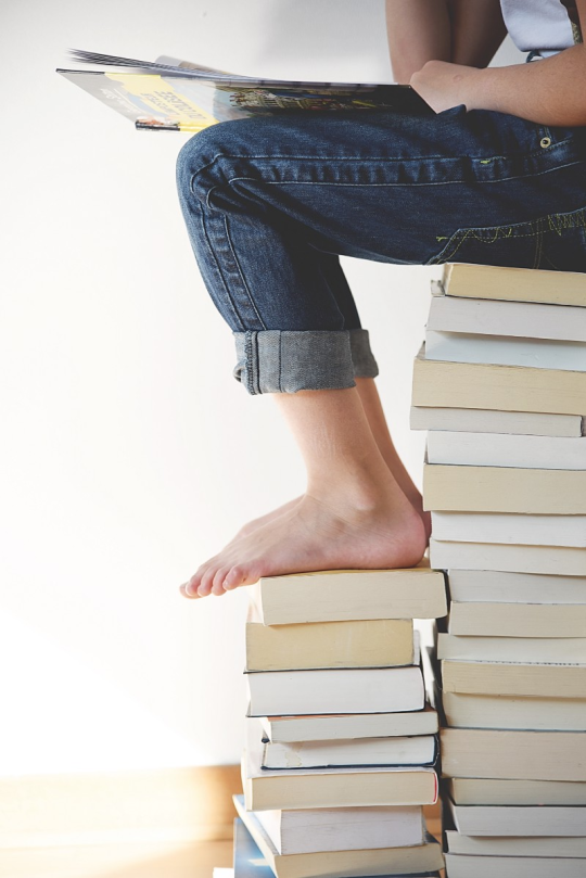 Child sitting on a stack of books reading